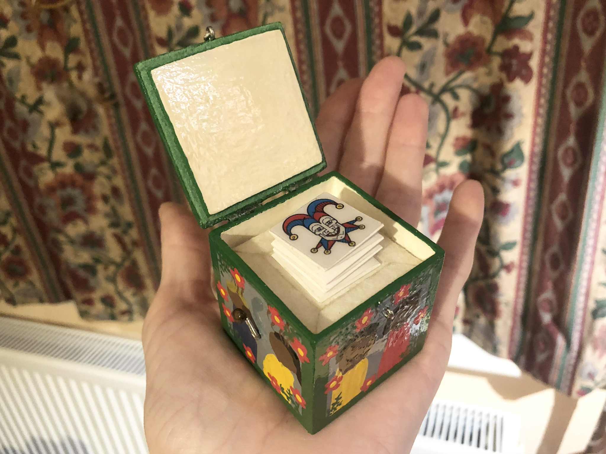 The latch opened, inside the box sits a sturdy paper spring, on top of which sits a jester's face, laughingly springing up from the inside.