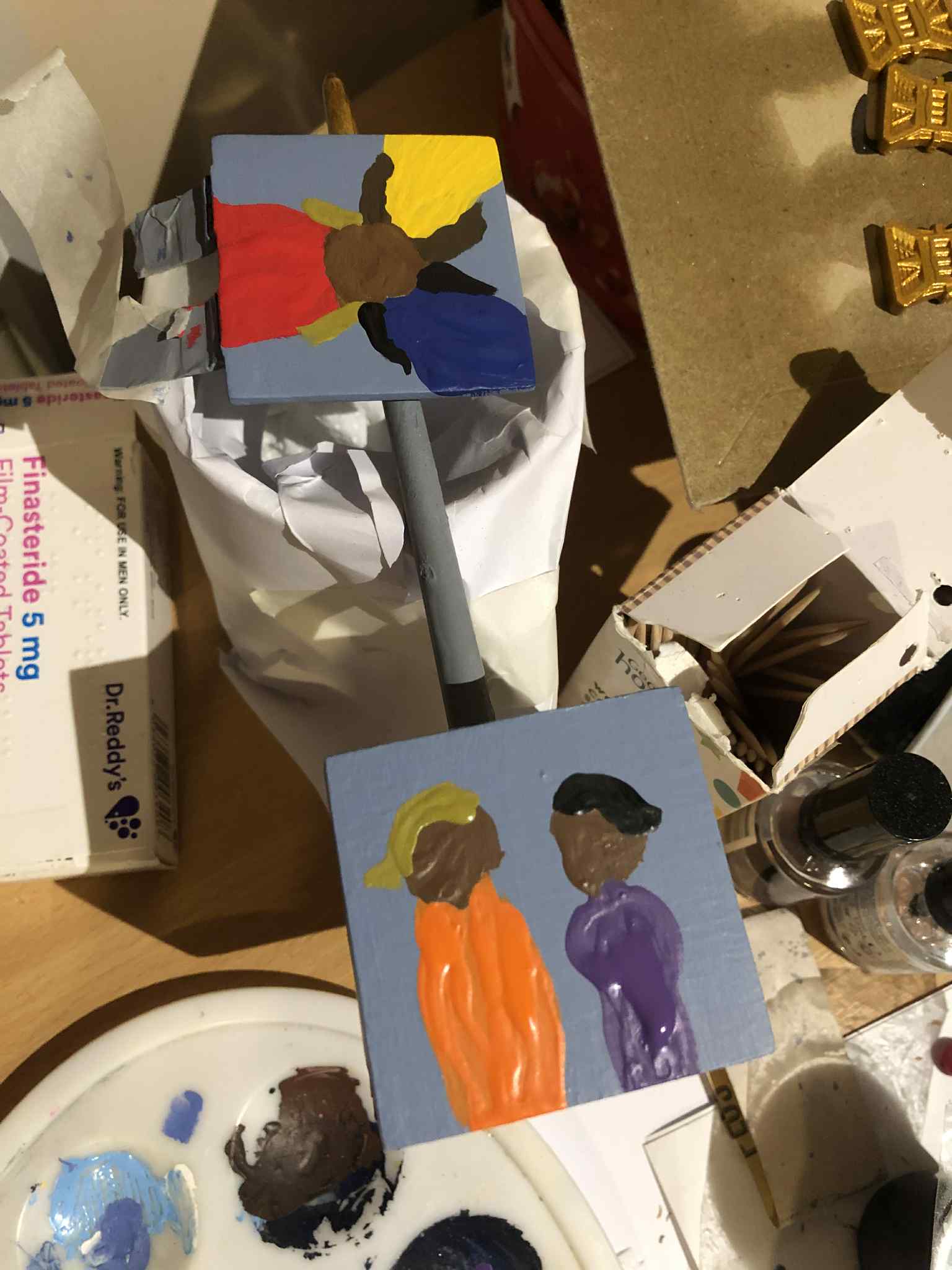 The cube, with the lid and box painted separately and left to dry after the thickly painted figures were put onto the sides, overtop of a very greyish light blue background.