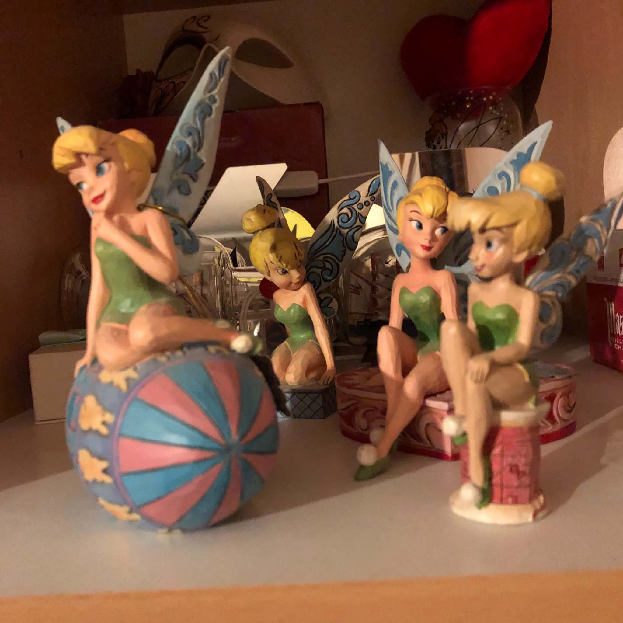 Four Tinkerbell statues on a shelf.