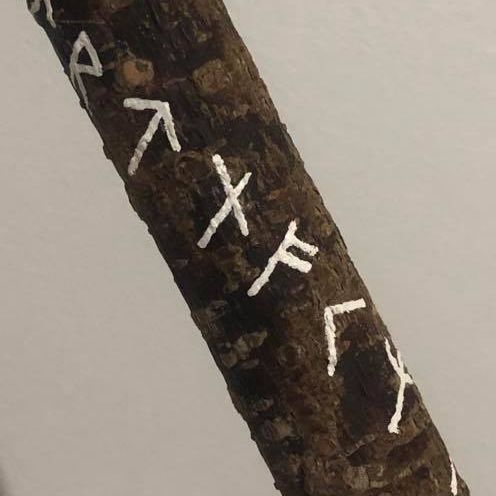 A mottled wooden staff with several runes painted on it