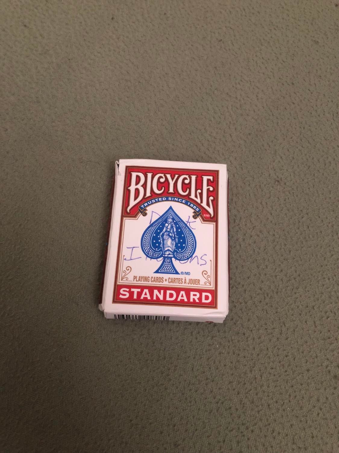A deck of bicycle cards, with Deck of Illusions written on the front, on a beige surface.