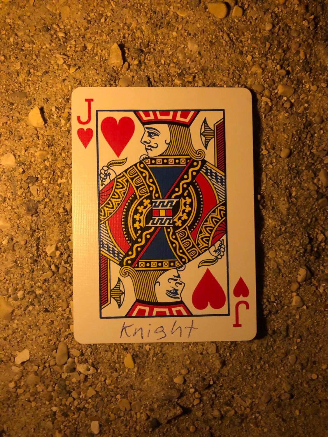 The jack of hearts with Knight written on it, laying on the darkened soil.