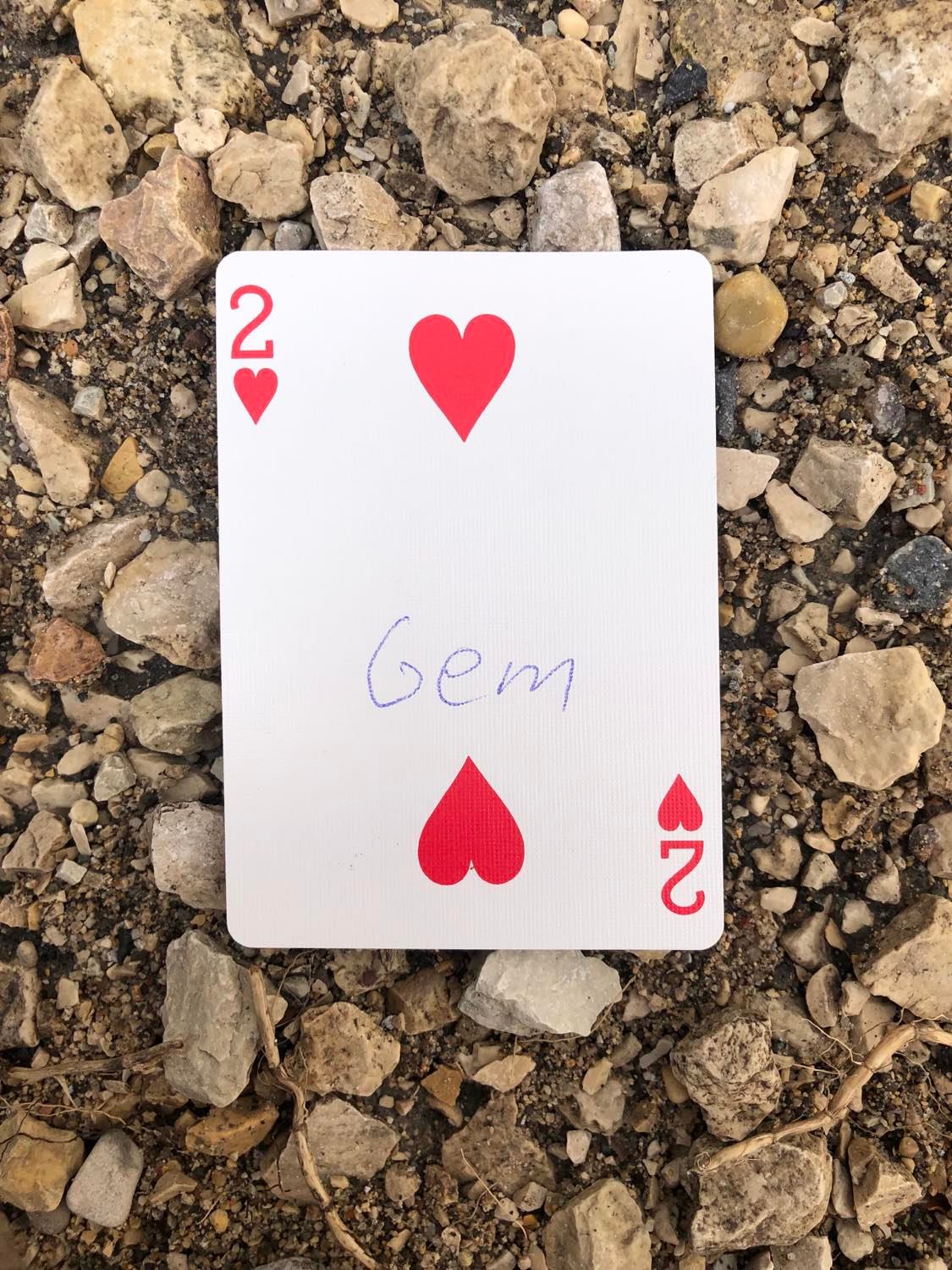 The two of hearts with Gem written on it, laying on the gravel path.