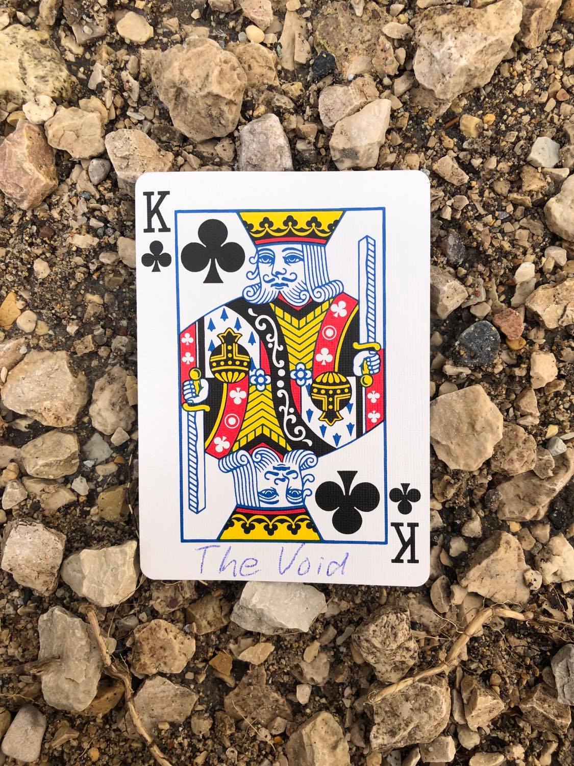 The king of clubs with The Void written on it, laying on the gravel path.