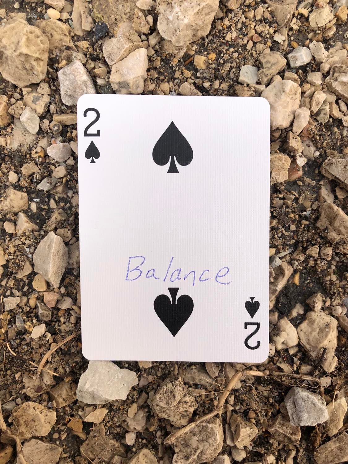 The two of spades with Balance written on it, laying on the gravel path.