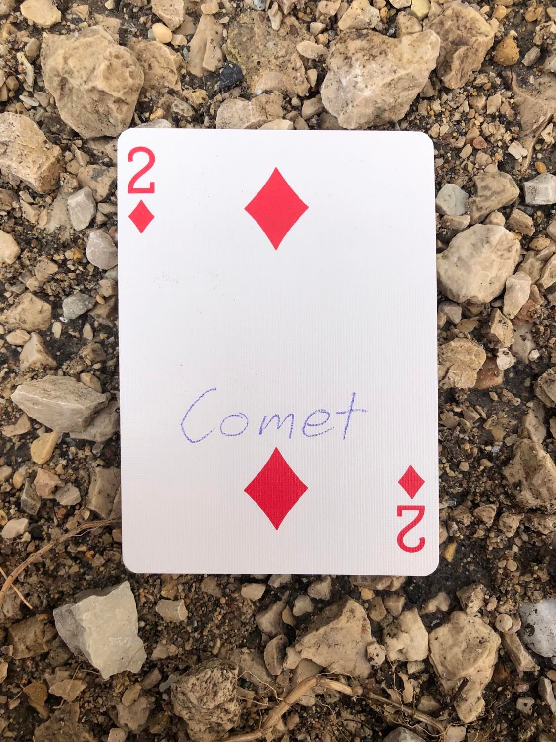 The two of diamonds with Comet written on it, laying on the gravel path.