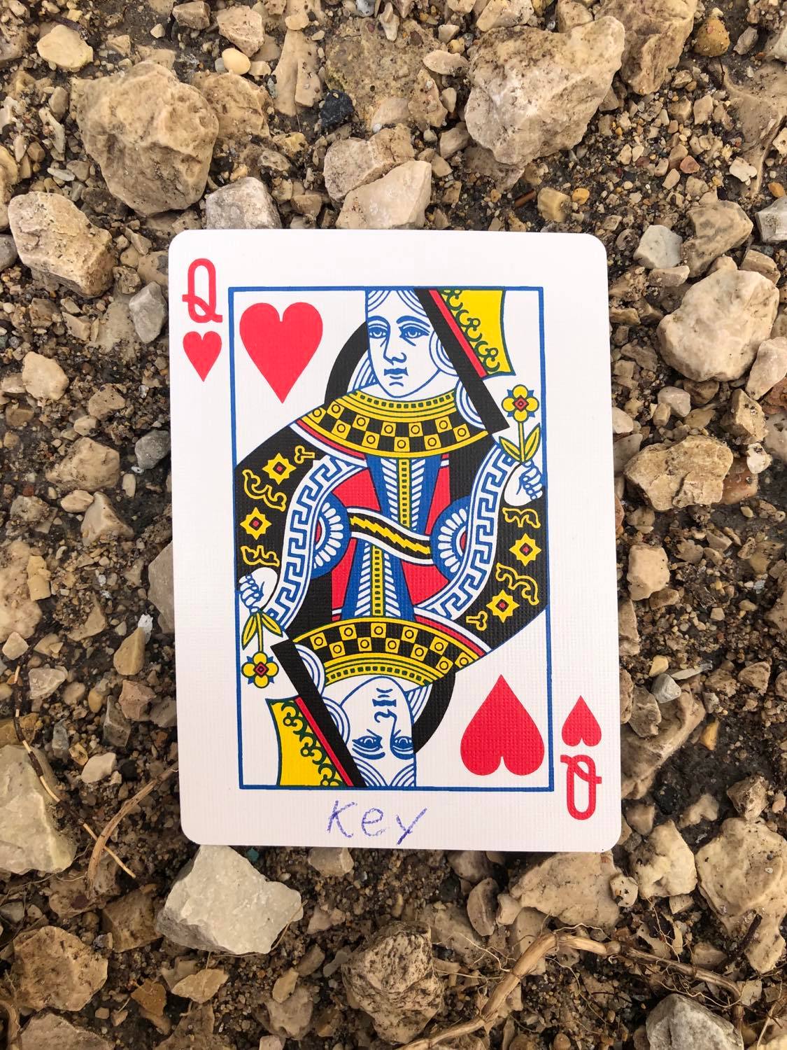 The queen of hearts with Key written on it, laying on the gravel path.