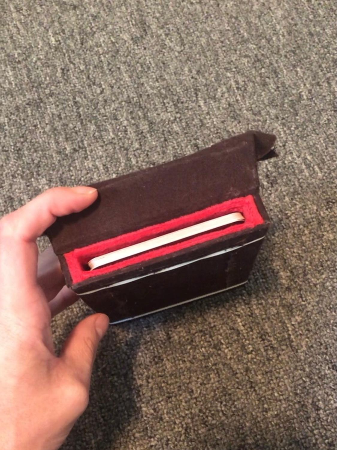 The box, now completely closed up, being held together with white elastics. The box is brown on the outside with the lip of a red lining showing, with the cards inside. It looks a little bit like a mouth, kinda muppet-like or something.