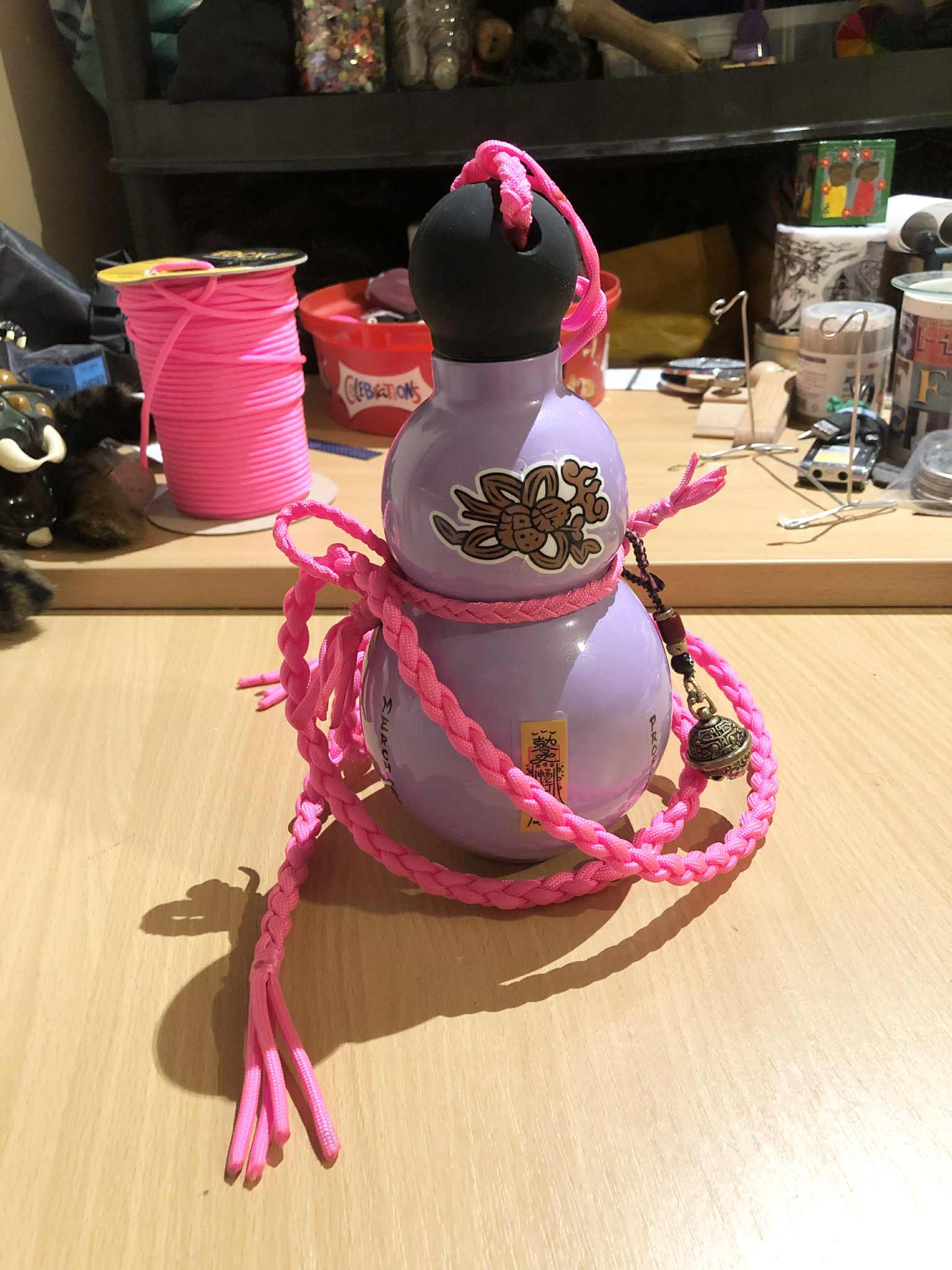 A lavender coloured gourd bottle depicting Japanese kanji for protection and balance, english text for Zebeth, and pink cords wrapped around it for carrying.