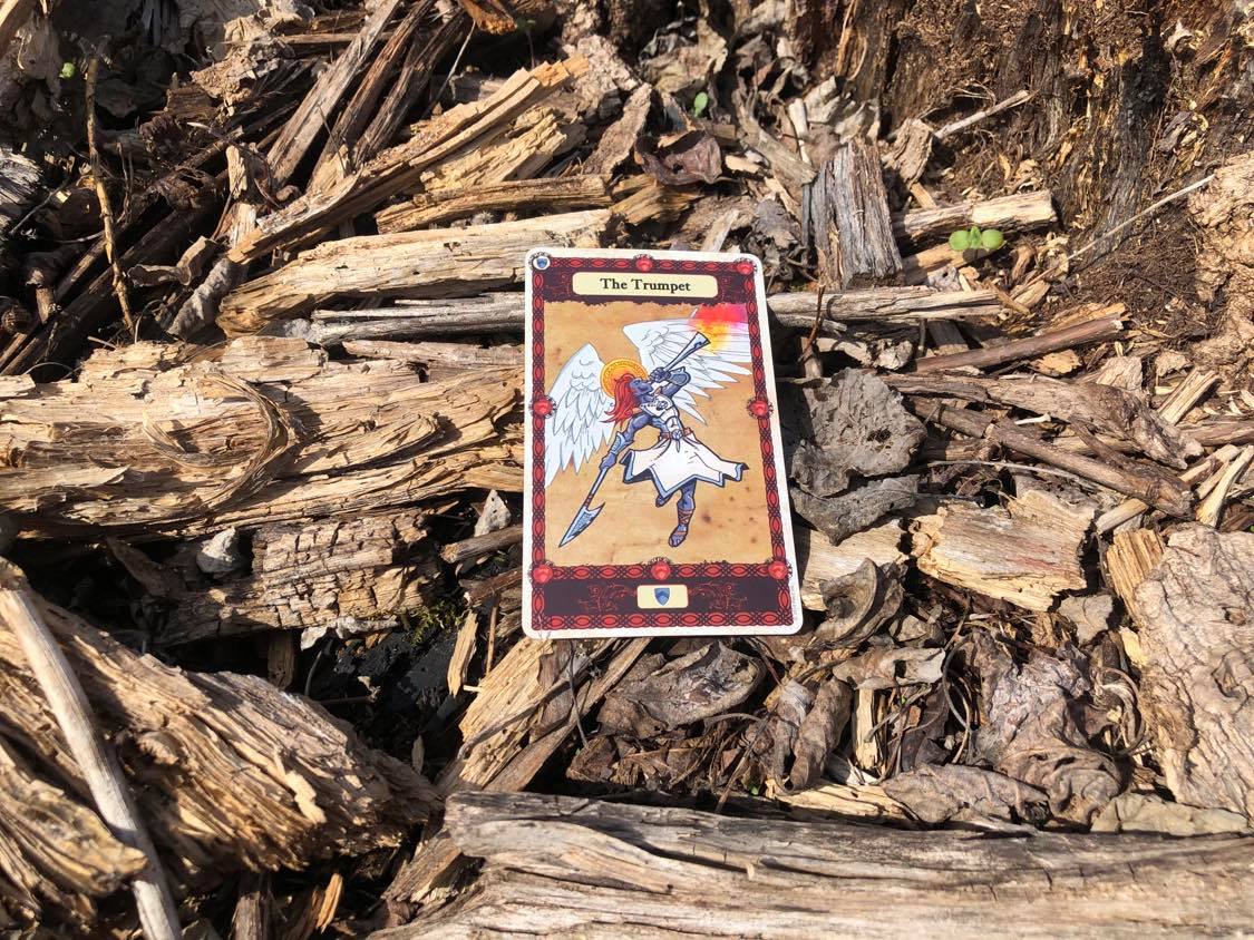 An angel blowing a trumpet, the card laying on the forest debris.