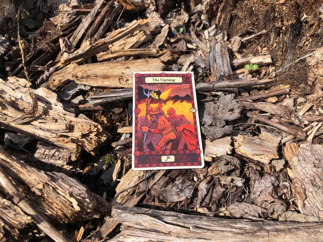 Figures holding pitchforks and torches, the card laying on the forest debris.
