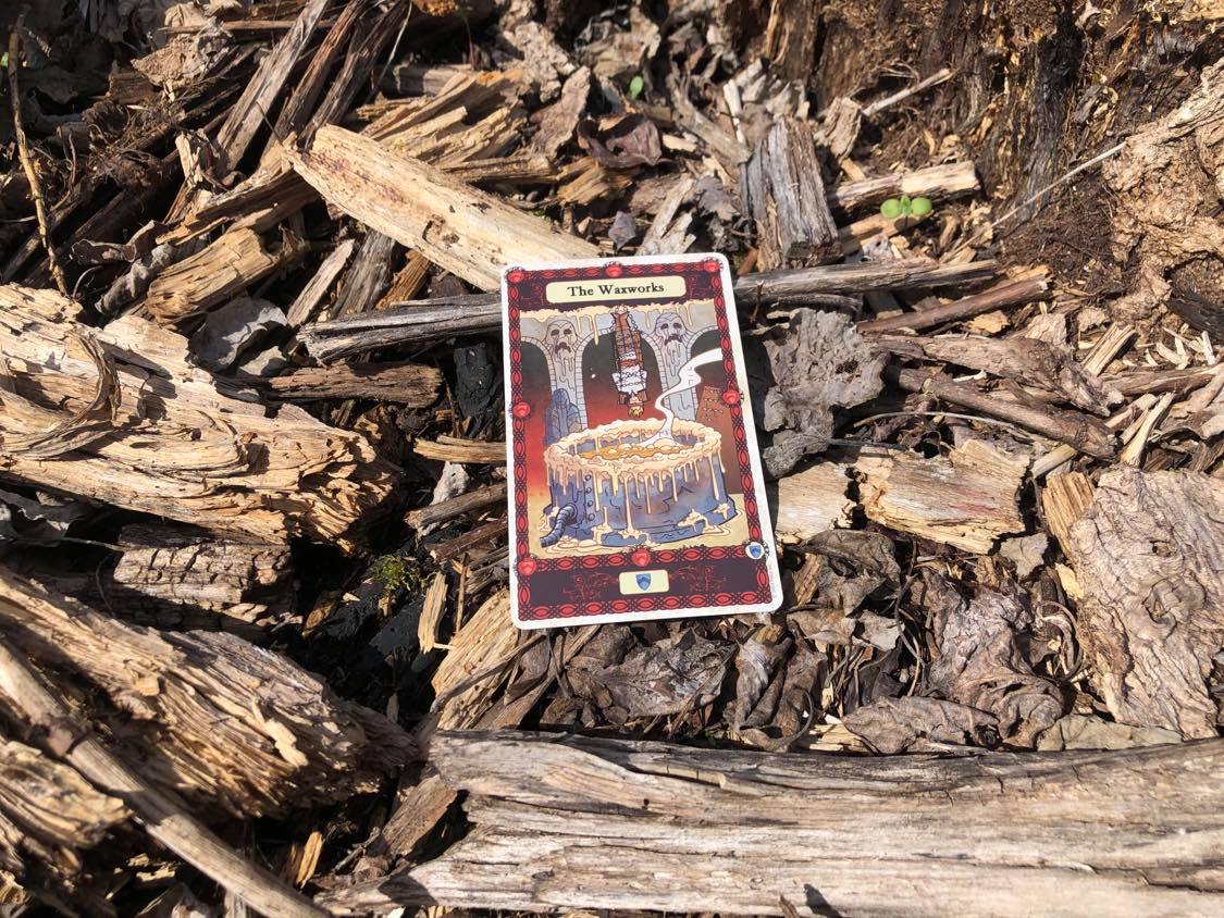 A bound man being dipped in a vat of wax, the card laying on the forest debris.