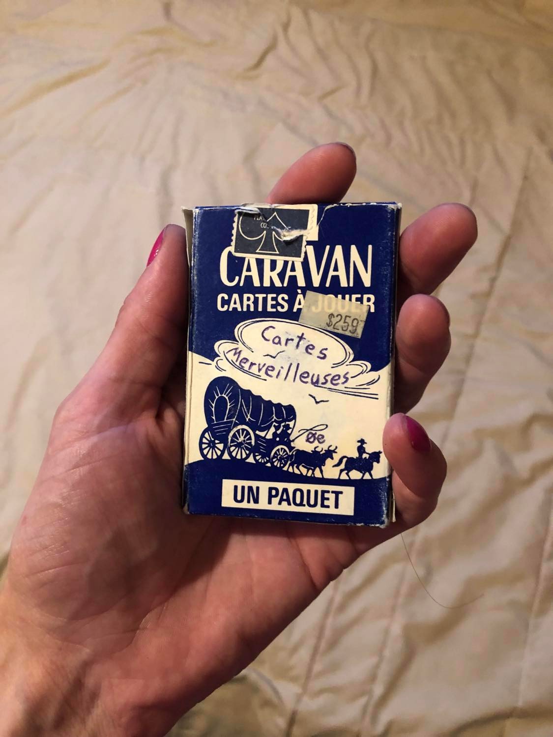The back of the box, showing it in French. It reads caravan, cartes a jouer, and the second half of the original sealing sticker, aged and worn, partially obscures it. The same covered wagon and oxen are there, and the clouds read Cartes Merveilleuses. '0e' is above the oxen, and it states itself as un paquet.