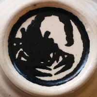 The bottom of a sake cup with a scorpion logo on the underside