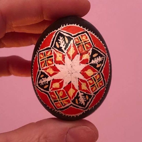 A painted easter egg, lots of reds and yellows, with wheat imagery on it.
