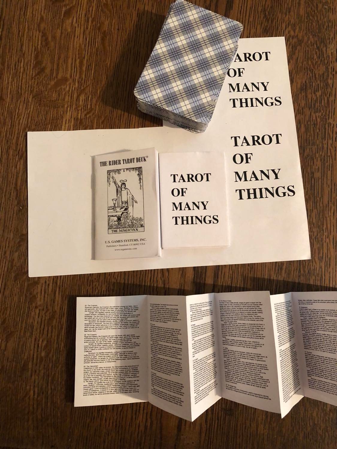A partially cut apart piece of paper, showing several potential sizes printed of the cover page (tarot of many things, in all caps and serif font, left-aligned on the page because it looked best that way. Kinda bold and plain, looks strong. Also an accordioning of the first handful of pages is sitting below it. Read the text below for details on that. Also the (pocket size) cards are sitting at the top of the pic.