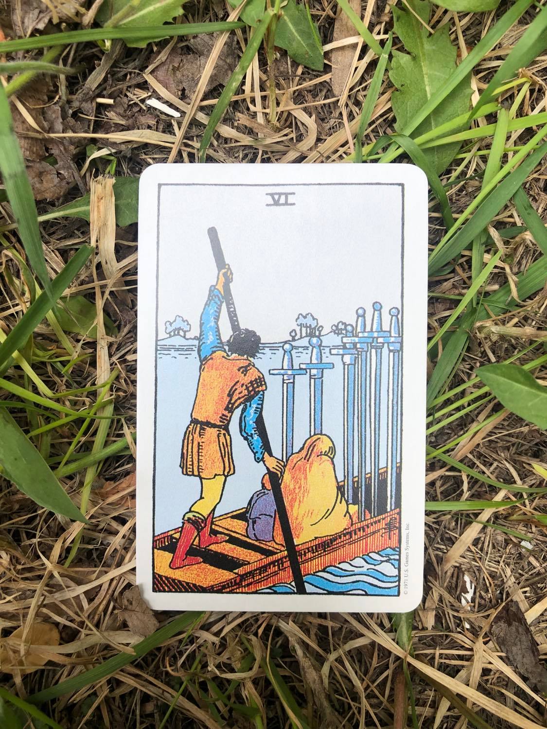 The Six of Swords, upright, laying in the grass.