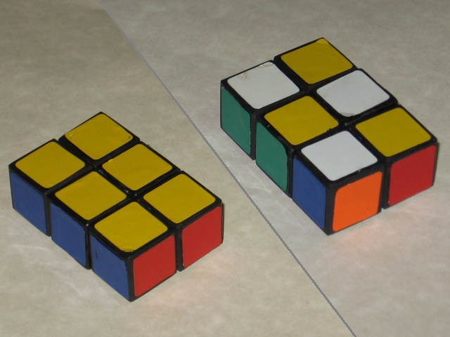 The 3x2x1 cube, with the old stickers applied, laying on the countertop. It's a split photo, with one side being solved, yellow blue and red showing, and one side scrambled.
