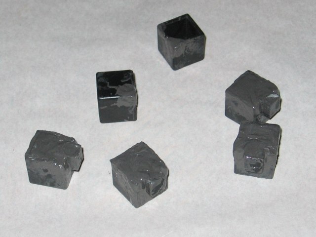 Several of the cubies, either partially or mostly covered in grey jb weld, sitting on a sheet of parchment paper.