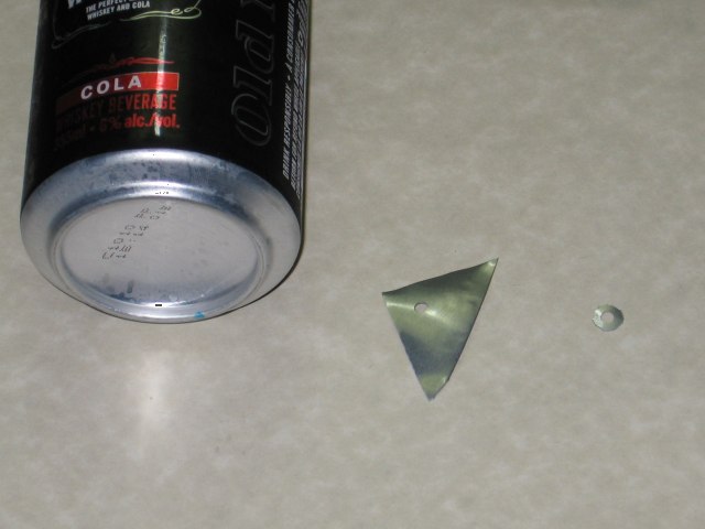 An empty cola can, beside a little triangle of aluminium, beside a little tiny metal washer made from it.