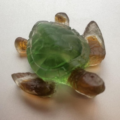 A translucent glass turtle sitting on a silver surface.