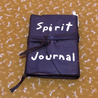 A leather book that says Spirit Journal laying on a gold patterned cloth