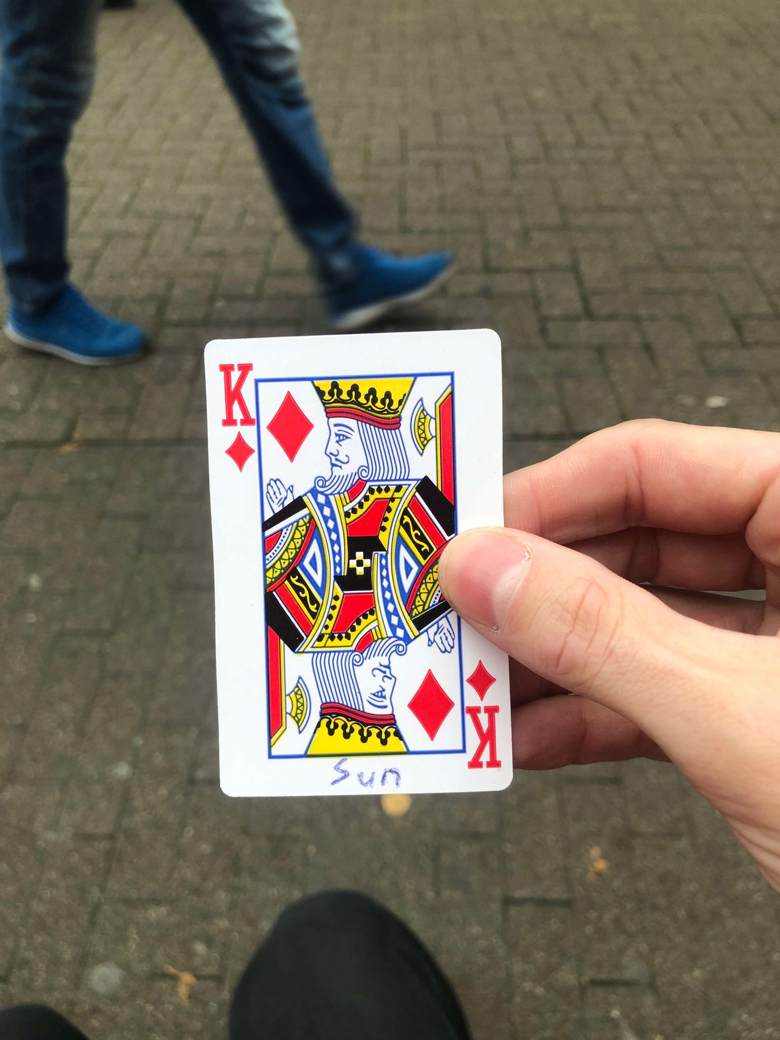 Sitting on a bench, a brick walkway in front of you, you hold the drawn card in front of you.