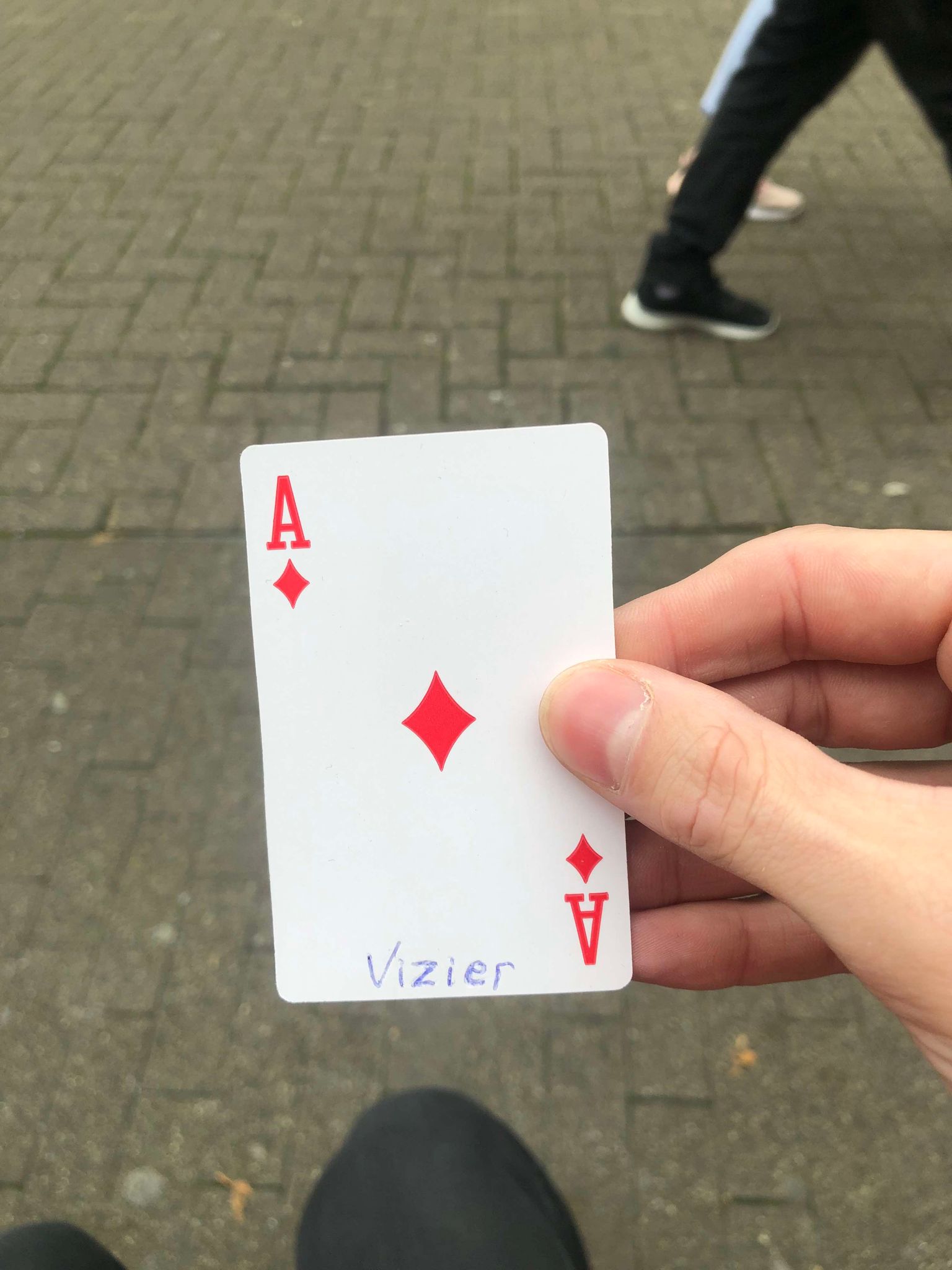 Sitting on a bench, a brick walkway in front of you, you hold the drawn card in front of you.