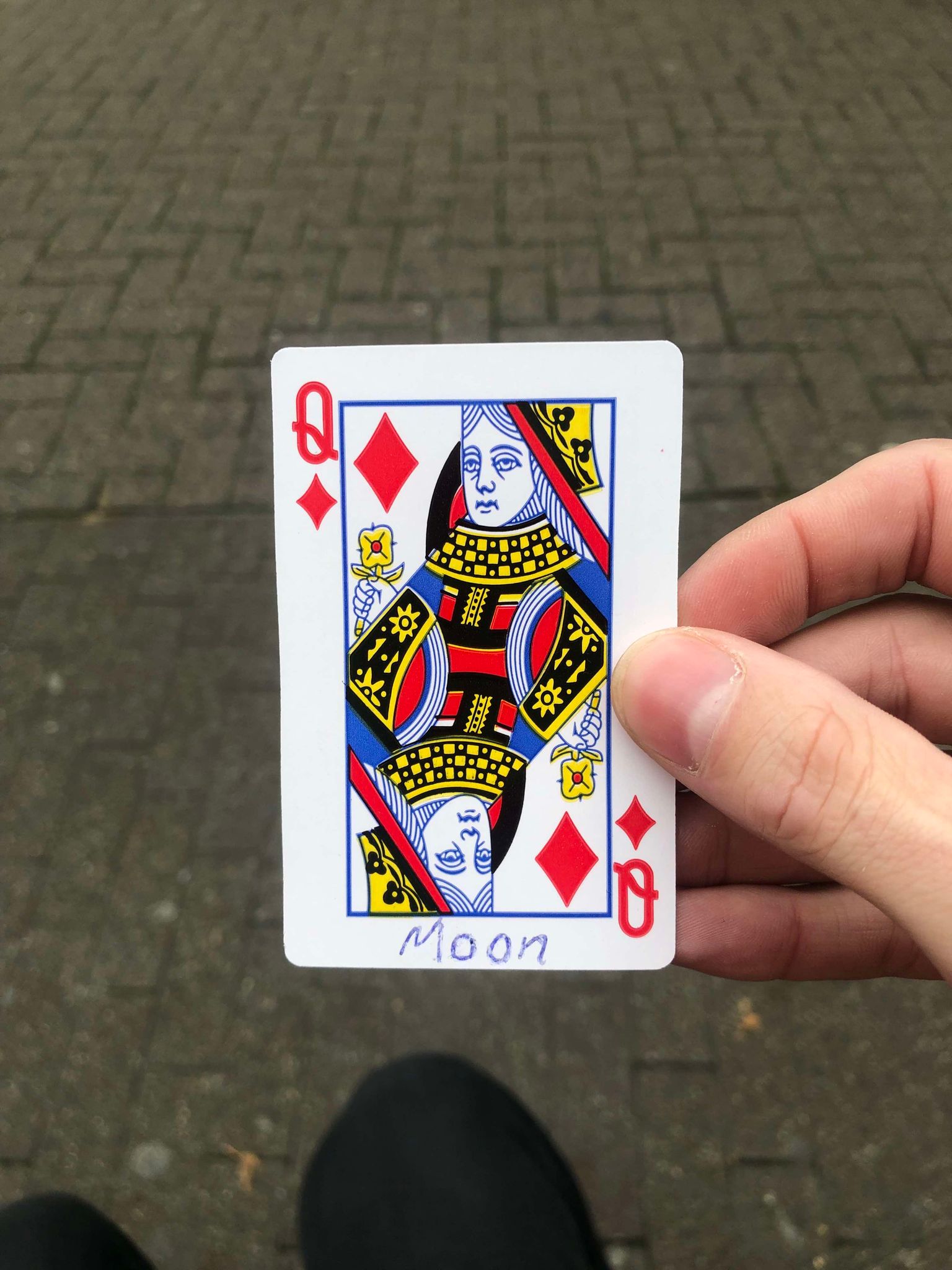 Sitting on a bench, a brick walkway in front of you, you hold the drawn card in front of you.