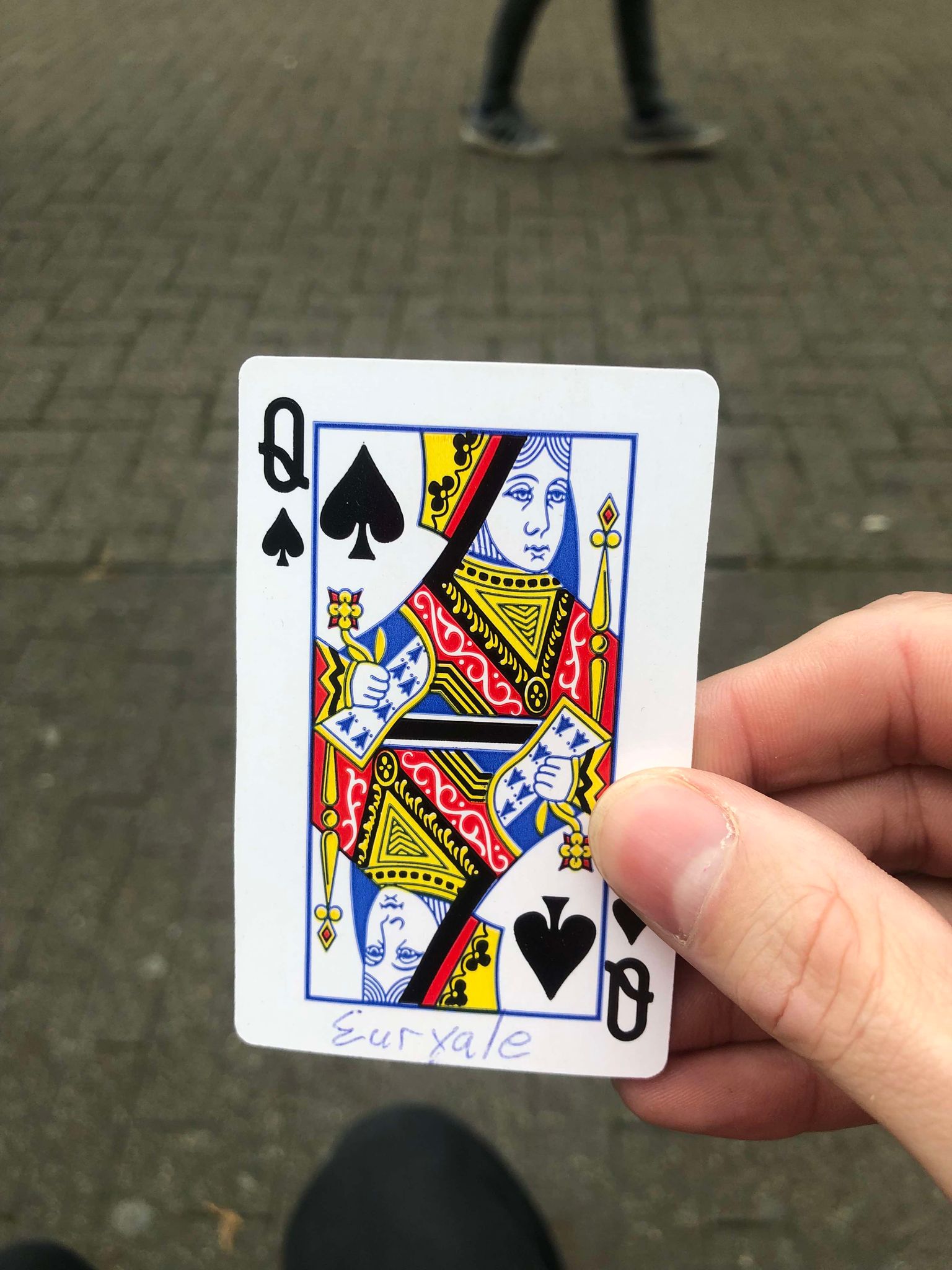 Sitting on a bench, a brick walkway in front of you, you hold the drawn card in front of you.