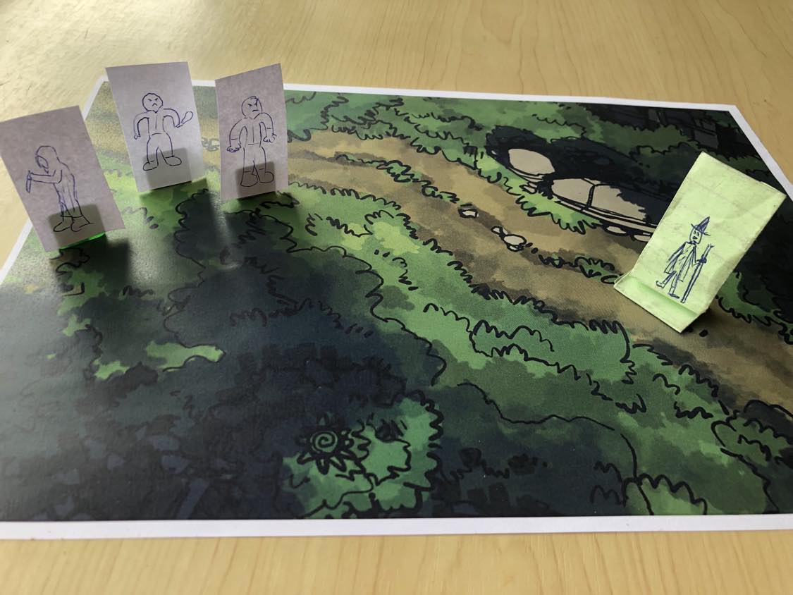 A battle map on a wooden table, three hand drawn bandits, two thugs and one cloaked figure with a knife, emerge from a clearing in the trees and begin to approach you as you walk down the path through the forest.