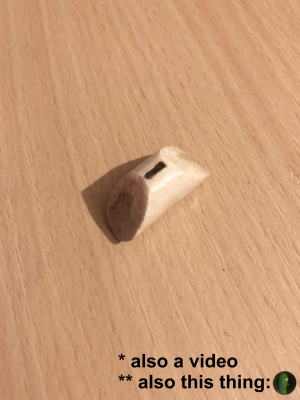 A photo of the one sided dice, a white wooden stick about two centimeters long, cut at opposite angles on either side so that the 1 is on the smallest side, and it will naturally roll to have that facing up. There is also some vine type lining running through the stick, which is kinda cool.
