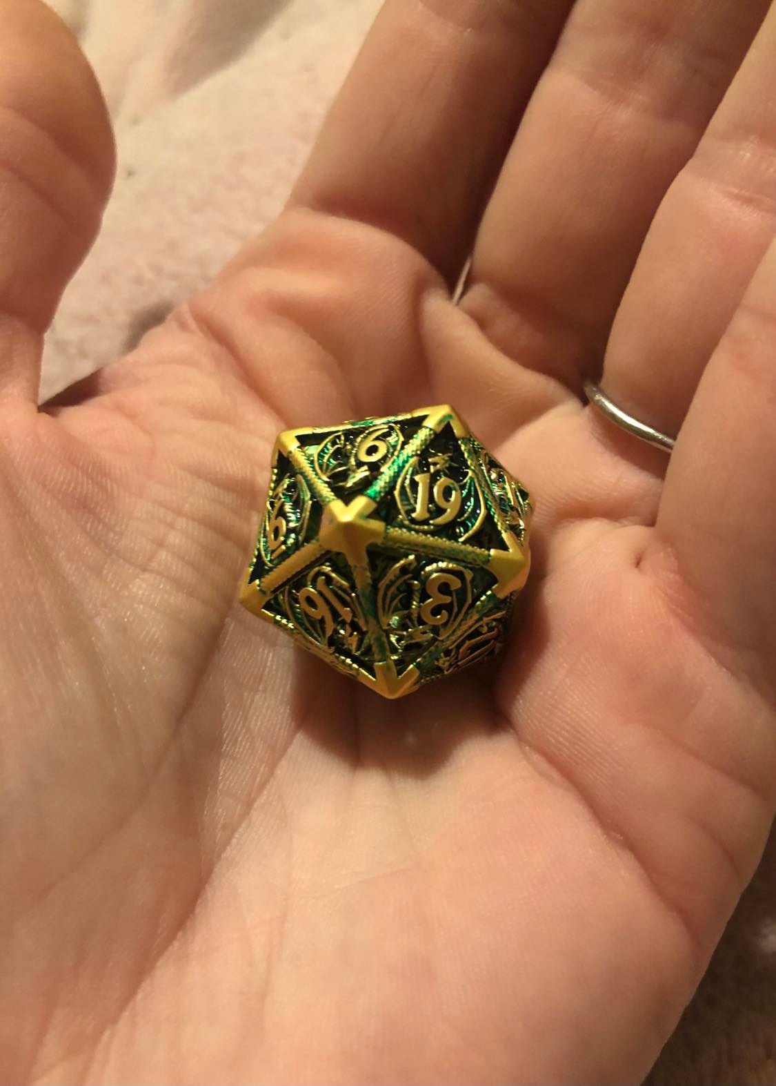 A closeup of the hollow metal dragon dice, showing each face as being a green dragon with wings outspread, and the number over the front of the dragon.