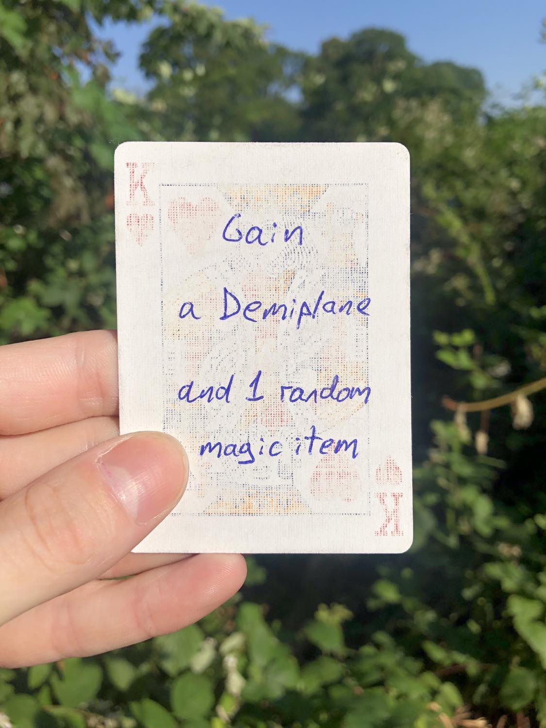 The king of hearts, held with the trees and foliage behind. Gain a Demiplane and 1 random magic item.