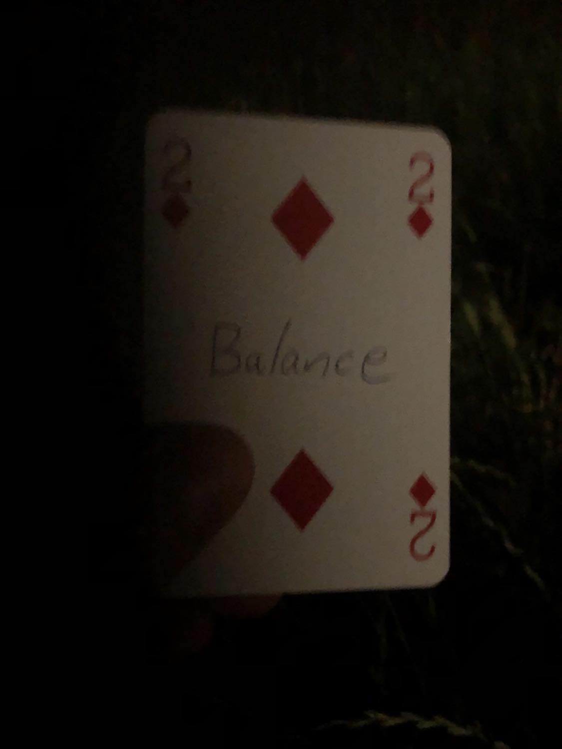 The two of diamonds with the word Balance written on it, held in the barely lit dark.