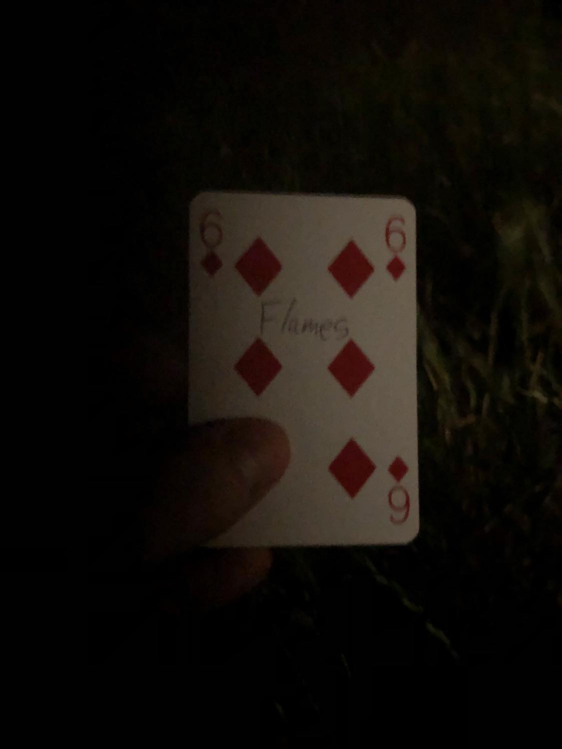 The six of diamonds with the word Flames written on it, held in the barely lit dark.