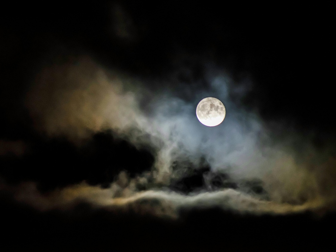A full moon shines through the light clouds in the night sky.