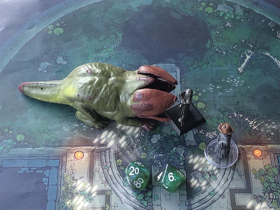 The battle map from above, with the monk fully attacking the creature, and the sorcerer rolling a pair of d10 dice to determine the wild magic surge.