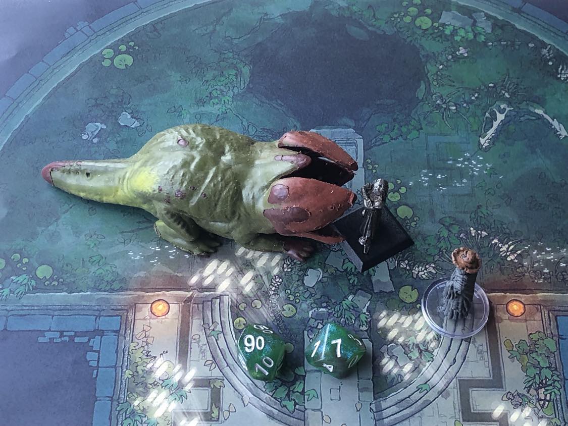 The battle map from above, with the monk fully attacking the creature, and the sorcerer rolling a pair of d10 dice to determine the wild magic surge.